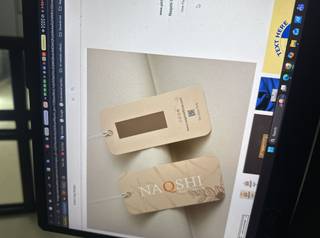 A laptop screen displaying two beige tags with strings, showing text and patterns, with browser tabs visible on top.